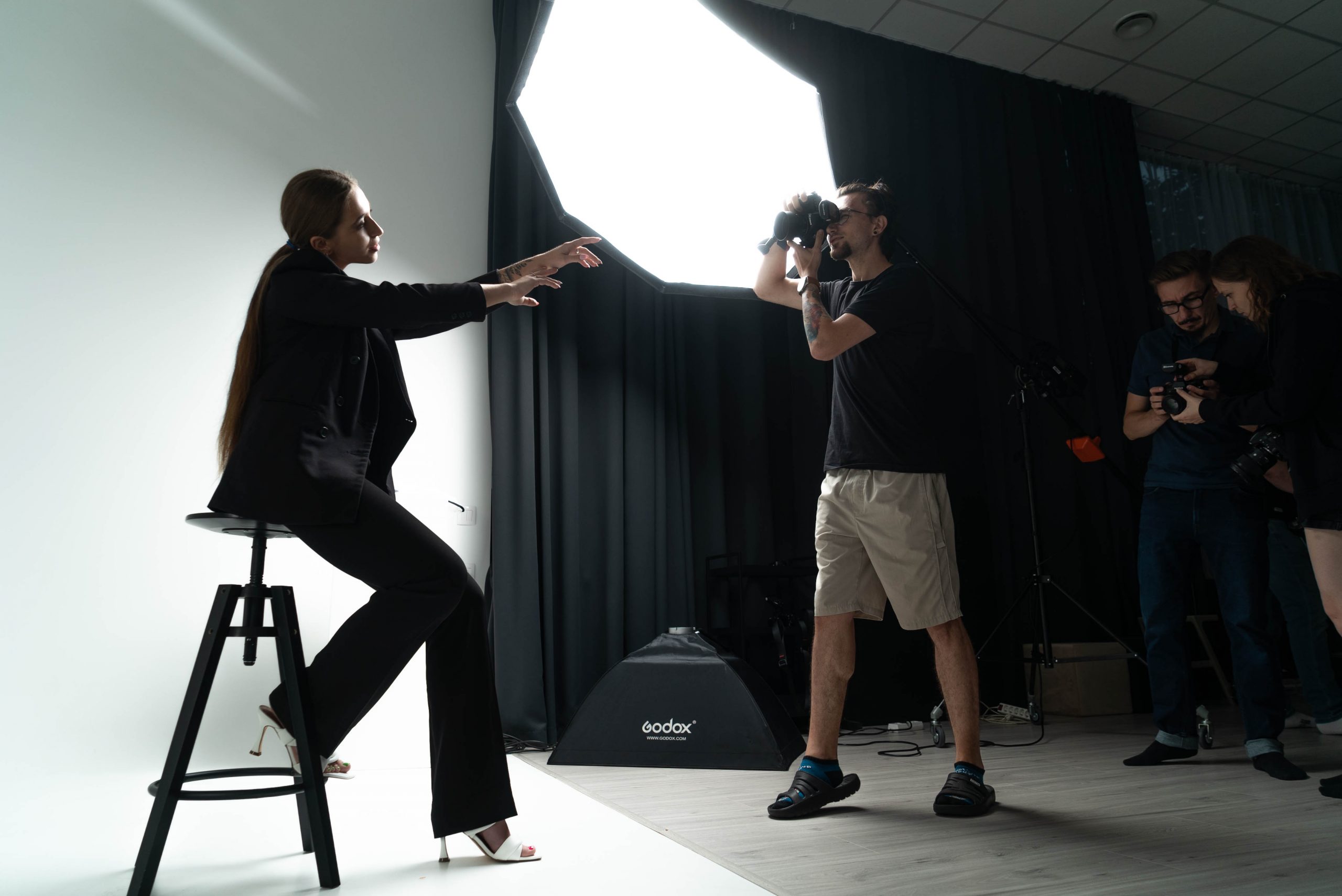 Modelka siedząca na cykloramie i fotograf robiący zdjęcie z lampą światła stałego